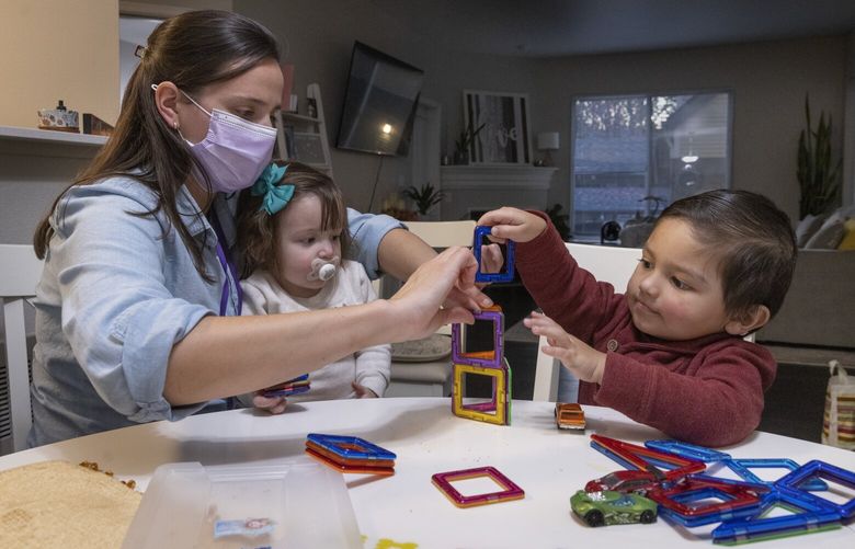 Kindering speech and language pathologist Kaitlyn McClain (l) helps almost three-year-old Steve, who has been slow to speak, build a structure with magnets in the family’s Issaquah home Tuesday, November 15, 2022.  She is holding his sister, Kamilah, 18 months.  Steve also has behavioral issues, which another therapist is working on in different sessions.   Kamilah is also receiving therapy at different times. She was slow to crawl and walk, but just started walking. 

 222155