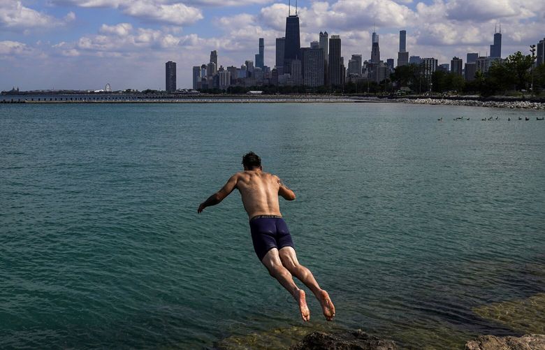 FILE – A man jumps into Lake Michigan to cool off on July 20, 2022, with the downtown Chicago skyline seen in the background. Studies predict the Great Lakes and other large freshwater bodies around the world will move toward acidity as they absorb excess carbon dioxide from the atmosphere, which also causes climate change. Experts say acidification could disrupt aquatic food chains and habitat. (AP Photo/Kiichiro Sato, File) NY473 NY473