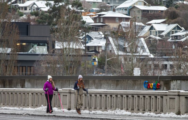Lacee Sherman, left, and Natalie Blake use ski poles to help navigate the icy sidewalks in Fremont on Friday, Dec. 23, 2022. They were walking from North Queen Anne to a friend’s house because they had agreed to take care of the friend’s dog.