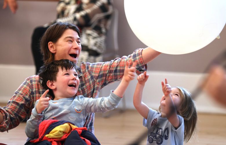 Anna Sherwood with her children Arne Stednick, 6, and Miriam Stednick, 2, reach out to tap a large balloon back into the circle of kids and their parents during a performance by The Harmonica Pocket at the Kindiependent Kids Rock Series at the Mount Baker Community Club in Seattle on December 31, 2022. For more information on upcoming Kindiependent concerts at the Mount Baker Community Club please check out https://www.mountbaker.org/kindiependent 222596