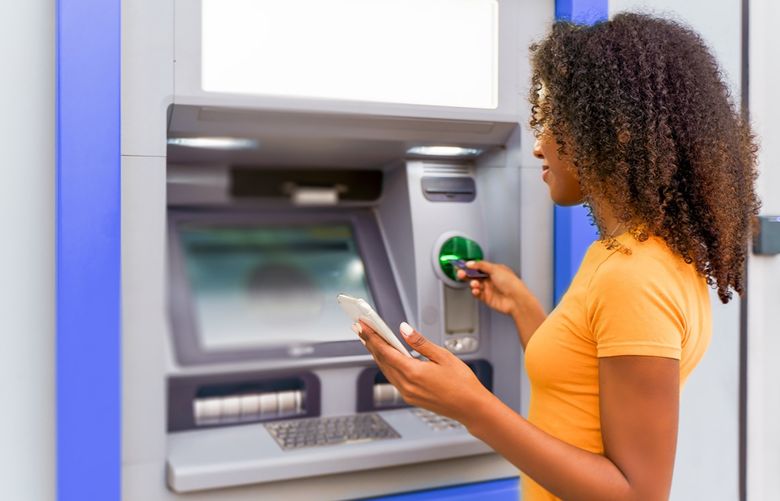 A woman with curly hair wearing an orange shirt uses an ATM machine.