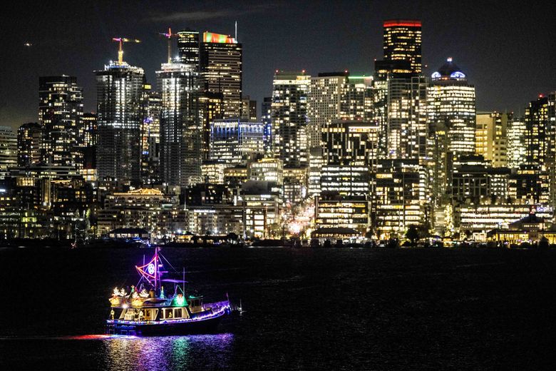 The cityscape lights the night sky as a boat decorated for the holidays passes by on Lake Union on Dec. 21, 2022. (Daniel Kim / The Seattle Times)