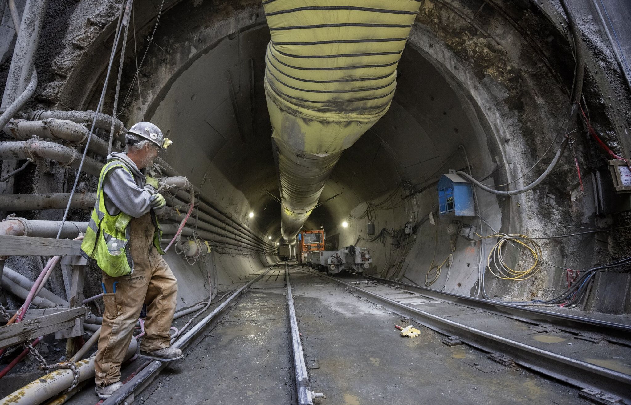 A construction worker speaks with the operator of a train that is pushing a flat car to pick up more segments to build walls in the tunnel at a drop shaft in Ballard last week.   (Ellen M. Banner / The Seattle Times)