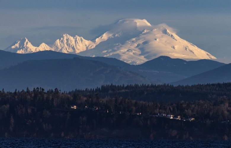 Homes are dwarfed by Mount Baker rising in the background, aglow during sunrise, Tuesday Jan. 10, 2023, seen from Possession Sound off Everett. After Tuesday’s stellar weather, rains are expected to return to the region, adding to an already gorgeous snowpack.