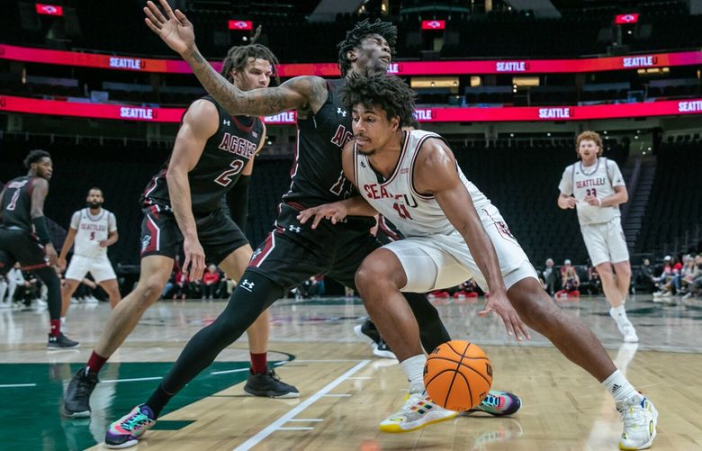Seattle’s Riley Grigsby drive the baseline with New Mexico State’s Doctor Bradley defending and New Mexico State’s Issa Muhammad, far left, looking on Thursday night at Climate Pledge Area in Seattle, Washington on January 12, 2023. The Hawks are tied with the Aggies 24-24 at the half.