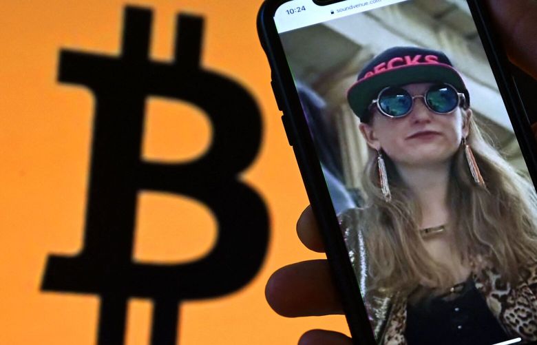 This illustration photo shows Heather Morgan, also known as “Razzlekhan,” on a phone in front of the Bitcoin logo displayed on a screen, in Washington, DC, February 9, 2022.  Photographer: Olivier Douliery/AFP/Getty Images