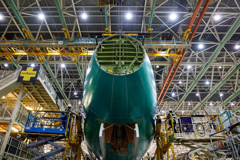 Two employees on scissor lifts sandwich the nose section of the final 747 before it is joined to the wing section during the final body join. The open doors on the bottom are where the nose landing gear will go. (Jennifer Buchanan / The Seattle Times)