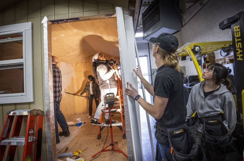 Students at the Advanced Manufacturing Skills Center presented by Edmonds College at Paine Field in Everett build a tiny home in their class as part of a pre-apprentice program. Second from right is Patrick Farrell from Marysville, who is adding trim to the exterior of the building with the help of Ellie Fongemie of Camano Island. Inside the front door at right is Regina Lewis, who is adding caulk to the interior of the house. Left of Lewis is Angelica Subillaga of Everett, painting a wall. (Ellen M. Banner / The Seattle Times)