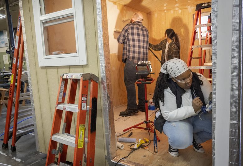 Regina Lewis of Kirkland, foreground, one of the students at the Advanced Manufacturing Skills Center class by Edmonds College at Paine Field in Everett, caulks around the door frame in a tiny home the students are building during their pre-apprentice program. (Ellen M. Banner / The Seattle Times)