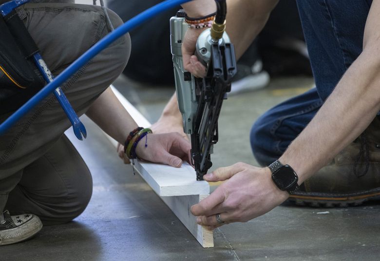 Patrick Farrell of Marysville, right, holds together boards that will be used for trim on a tiny house as fellow student Ellie Fongemie of Camano Island uses a nail gun to nail the pieces of trim together. (Ellen M. Banner / The Seattle Times)