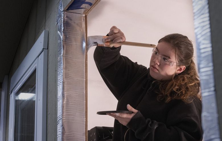 Chelsie Andrews of Stanwood paints an interior wall of the tiny house she and other students have built in their class as part of a pre-apprentice program at the Advanced Manufacturing Skills Center by Edmonds College at Paine Field in Everett. (Ellen M. Banner / The Seattle Times)