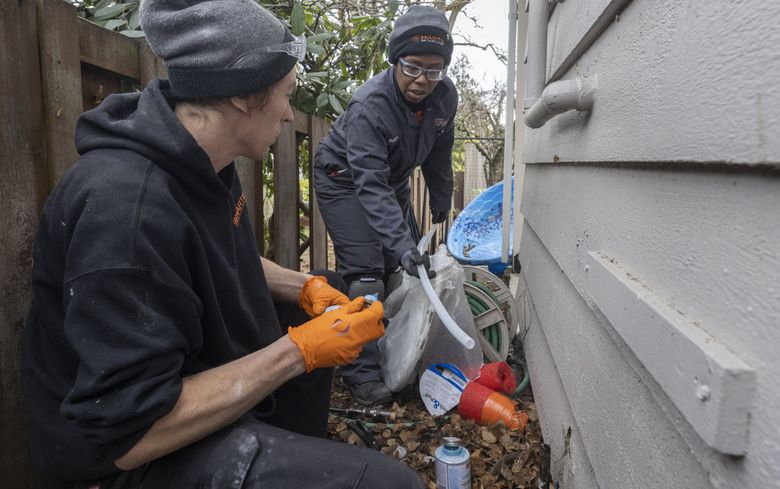 Tonya Miller, right, an apprentice plumber with Harts Services, hands a piece of PEX plastic tubing to journeyman plumber Will Lane as he hooks up the main water line to the interior of a Des Moines home. (Ellen M. Banner / The Seattle Times)