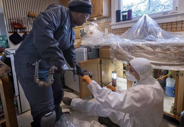 Tonya Miller, left, an apprentice plumber with Harts Services, takes a piece of galvanized pipe that apprentice Ricky Bui, who has been in the field longer than Miller, has just cut from beneath the kitchen sink of a Des Moines home. (Ellen M. Banner / The Seattle Times)