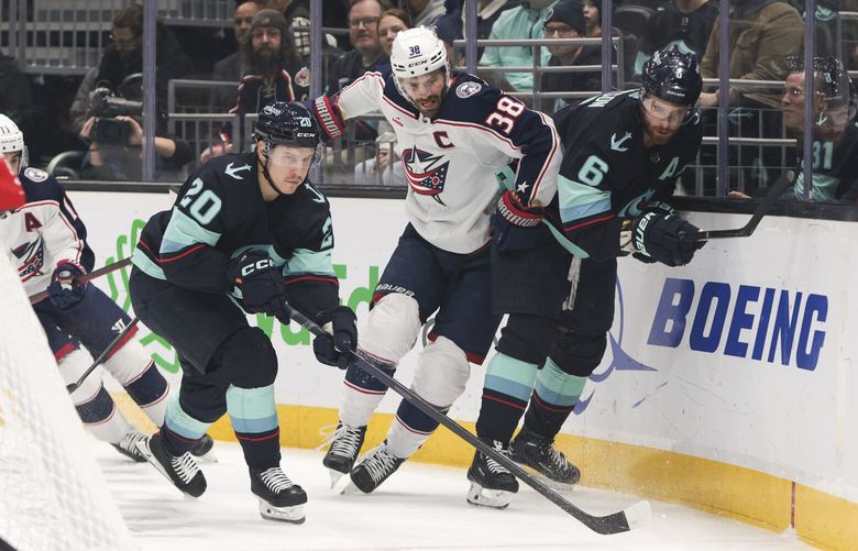 Columbus Blue Jackets center Boone Jenner (38) goes for the puck defended by Seattle Kraken right wing Eeli Tolvanen (20) and defenseman Adam Larsson (6) during the first period of an NHL hockey game Saturday, Jan. 28, 2023, in Seattle. (AP Photo/Jason Redmond)