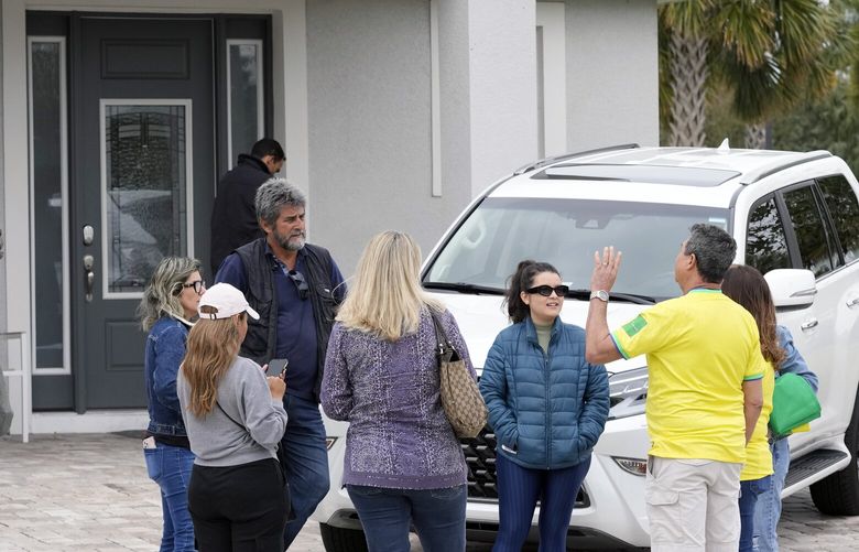 Supporters of former Brazilian president Jair Bolsonaro talk to a security guard asking for autographs from Bolsonaro outside the home where he is living Friday, Jan. 13, 2023, in Kissimmee, Fla. (AP Photo/John Raoux) FLJR102 FLJR102
