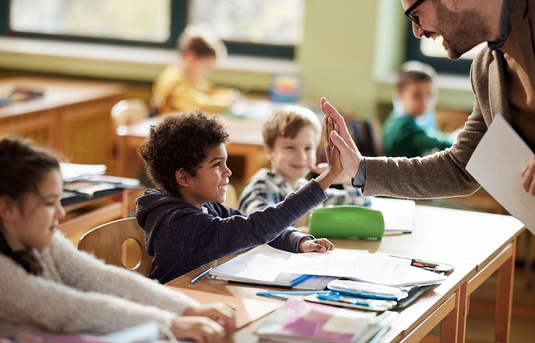 Happy male teacher giving high-five to his elementary student in a sun-filled classroom.