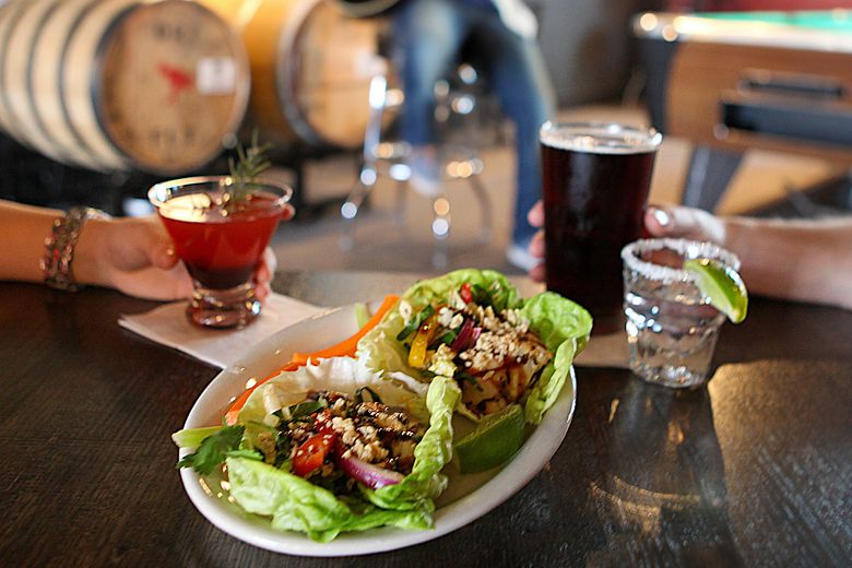 Lettuce wraps with ground meat and veggies on a table with cocktails in the background