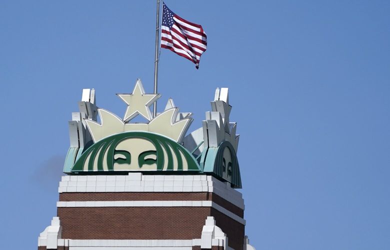 The U.S. flag flies above the Starbucks mermaid logo, Monday, April 26, 2021, at the coffee company’s corporate headquarters in Seattle. (AP Photo/Ted S. Warren) WATW101