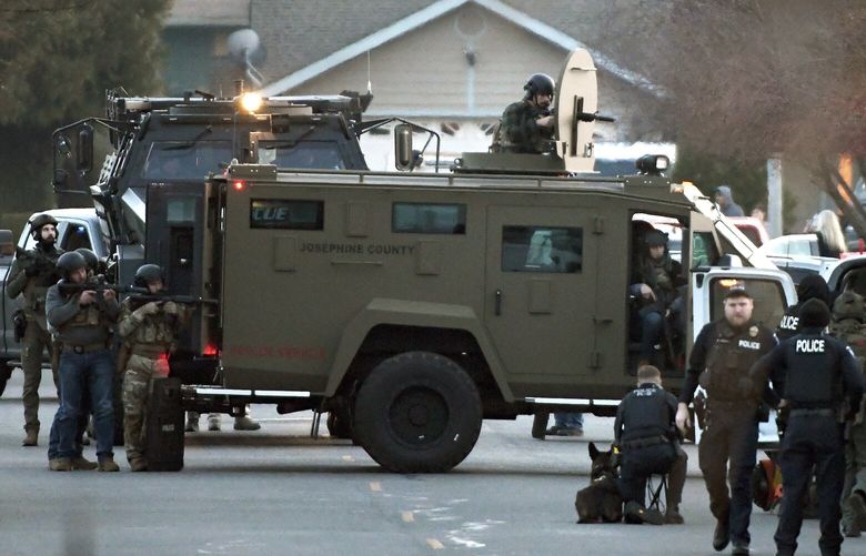 Law enforcement officers aim their weapons at a home during a standoff in Grants Pass, Ore., on Tuesday, Jan. 31, 2023. Police said the standoff involving a man suspected in a violent kidnapping in Oregon who was barricaded underneath the home has been “resolved.”   (Scott Stoddard/Grants Pass Daily Courier via AP) ORGRA601 ORGRA601