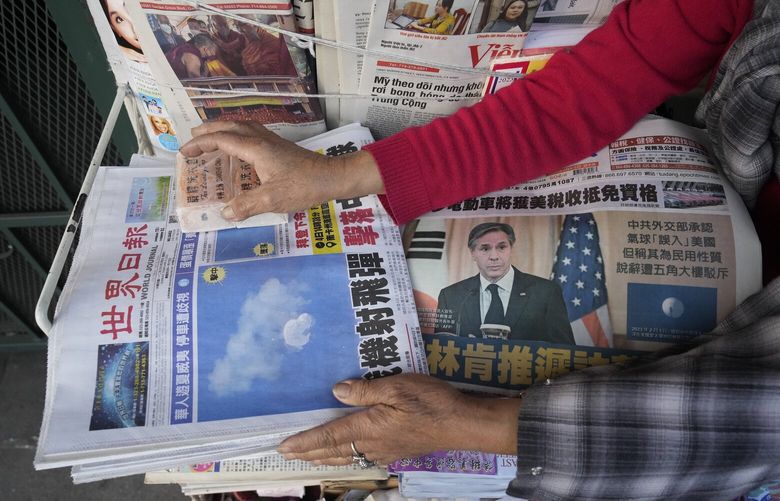 Business owner “Annie” weights down copies of the Chinese Daily News newspaper showcasing pictures of a suspected Chinese spy balloon, in the Chinatown district of Los Angeles Sunday, Feb. 5, 2023. The balloon’s presence in the sky above the United States before a military jet shot it down over the Atlantic Ocean with a missile Saturday has further strained U.S.- China ties. (AP Photo/Damian Dovarganes) CADD703 CADD703