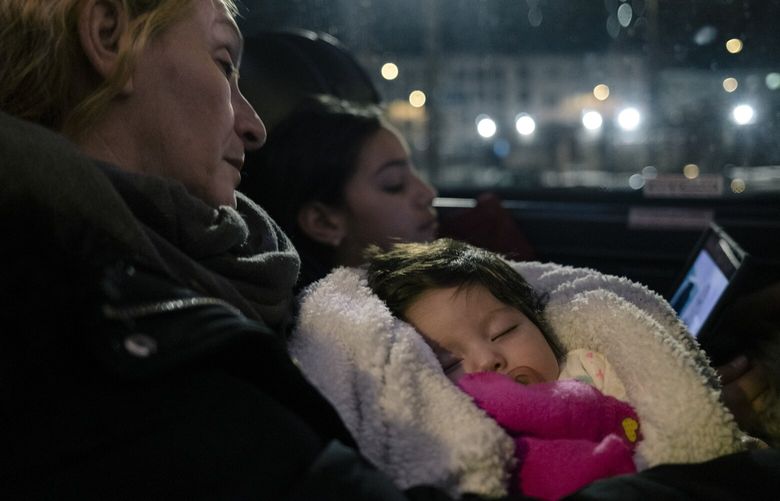 Elsa Brito, left, holds her two-month-old granddaughter, Amber Peña, as they sleep aboard a bus headed toward the border with Canada, in Albany, N.Y. on Feb. 5, 2023. New York City is buying bus tickets for migrants who want to seek asylum in Canada, where they hope to have an easier time getting work permits and health insurance. (José A. Alvarado Jr./The New York Times) XNYT109 XNYT109