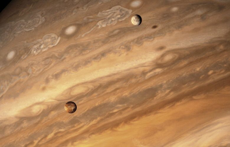 An undated photo provided by NASA of Jupiter’s moons Io, lower left, and ice-sheathed Europa, upper right, orbiting across the face of the giant planet. Researchers reported auroras around Jupiter’s two largest Galilean moons for the first time and found new features in the auroras of Io and Europa. (NASA via The New York Times) —NO SALES; EDITORIAL USE ONLY — XNYT93 XNYT93