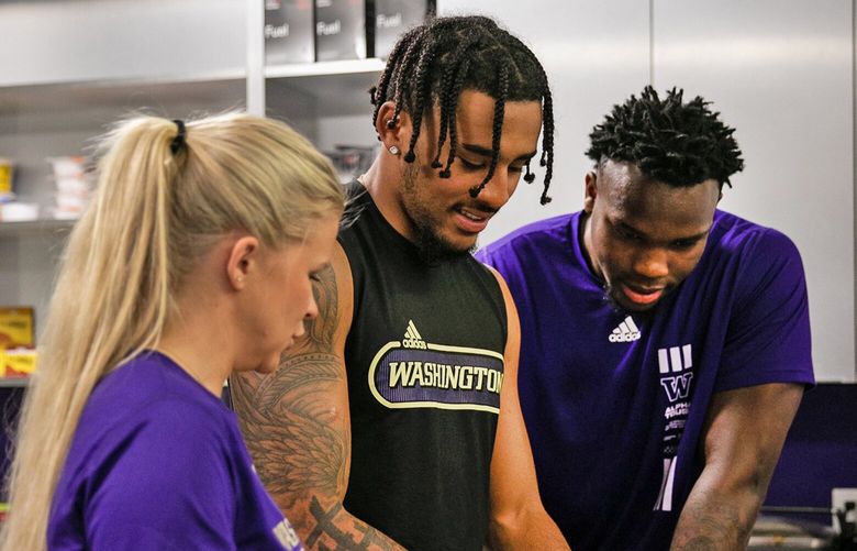 UW director of football performance nutrition Alison VandenBerghe assists wide receiver Taj Davis (center) and edge Jeremiah Martin (right) during a cooking class.