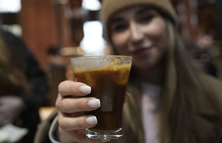Kaya Cupial, right, shows her Oleato Iced Cortado coffee at the Starbucks coffee shop in Milan, Italy, Monday, Feb. 27, 2023. (AP Photo/Antonio Calanni) 