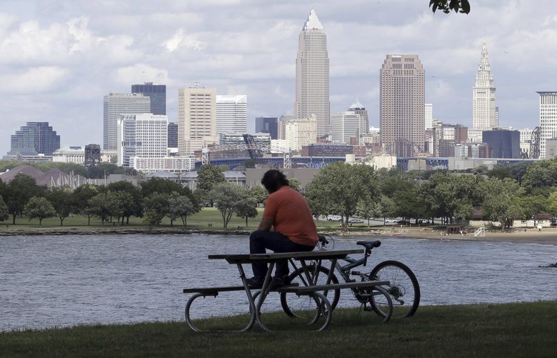 FILE – A man sits on a picnic table with a view of downtown Cleveland on July 8, 2014. Conservatives and conspiracy theorists are increasingly convinced the concept of a “15-minute city” is the latest nefarious plot to curtail individual freedoms. But urban experts and city officials say the design principle — recently embraced by cities including Oxford, England, Paris, and Cleveland, Ohio — is simply about building more compact, walkable communities where people are less reliant on cars. (AP Photo/Tony Dejak, File) NYAB410 NYAB410