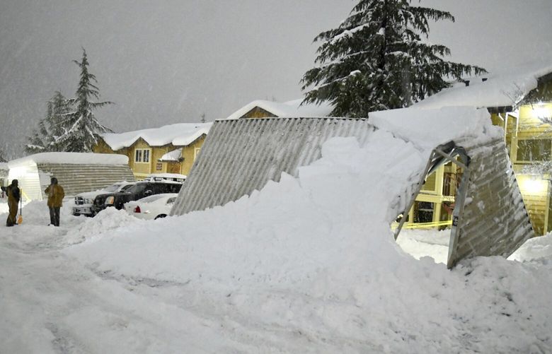 A pair of residents at the Cedar Park apartments in Grass Valley, Calif., take a break from shoveling snow during Tuesday evening’s blizzard conditions on Feb. 28, 2023, that caused widespread damage to the Sierra Nevada, including these awnings, which buckled from the snow. (Elias Funez/The Union via AP) CAGRA602 CAGRA602