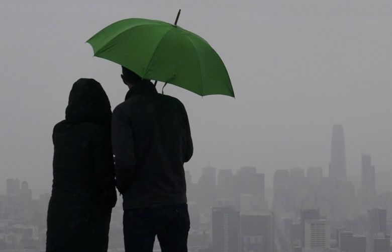 People stand under an umbrella while looking toward the skyline from Twin Peaks in San Francisco, Thursday, March 9, 2023. California is bracing for the arrival of an atmospheric river that forecasters warn will bring heavy rain, strong winds, thunderstorms and the threat of flooding even as the state is still digging out from earlier storms. (AP Photo/Jeff Chiu) CAJC401 CAJC401