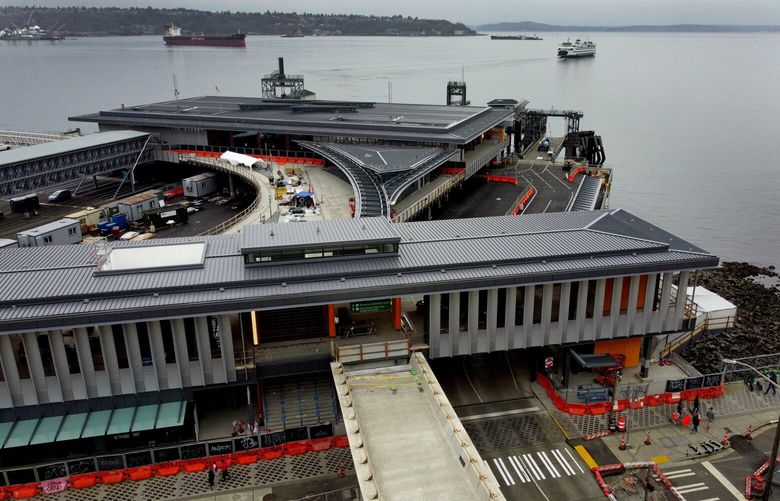 Colman Dock’s new entry building and permanent pedestrian elevated walkway along Marion Street, all set to open in 2023, is seen from the air, Sunday, March 12, 2023 in Seattle. The current in-use elevated pedestrian walkway (not pictured), south of this new bridge, will be taken down. In the background, the MV Wenatchee ferry departs Colman en route to Bainbridge Island.