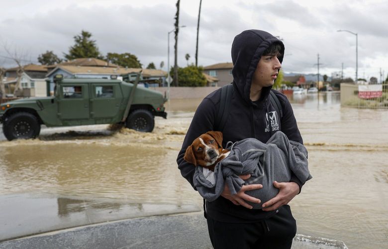 Esteban Sepulveda holds his dog Milo while leaving his home in Pajaro Valley, Calif., Sunday March 12, 2023. Wet, miserable weather continued across huge swaths of California on Sunday as an atmospheric river that caused major flooding flowed eastward, and as a new system threatens the region with another onslaught of rain, snow and gusting winds as soon as Monday night. (Shae Hammond/Bay Area News Group via AP) CAJOS701 CAJOS701