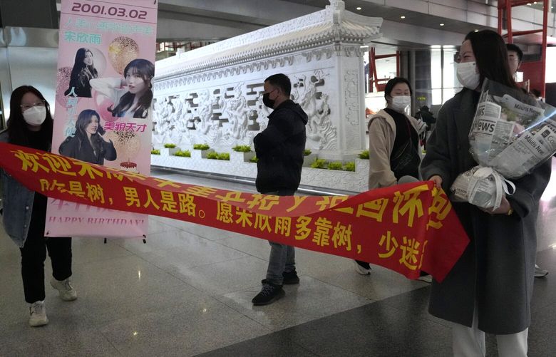 Women unfurl a banner to welcome their friend back at an exit for passengers arriving at the Beijing Capital International Airport in Beijing, Tuesday, March 14, 2023. China will reopen its borders to tourists and resume issuing all visas Wednesday after a three-year halt during the pandemic as it sought to boost its tourism and economy. (AP Photo/Ng Han Guan) XHG104 XHG104