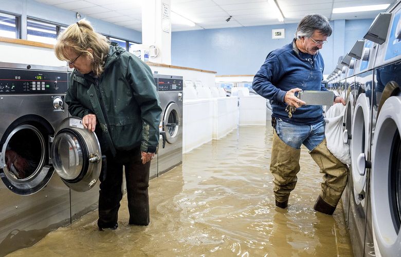 Pamela and Patrick Cerruti empty coins from Pajaro Coin Laundry as floodwaters surround machines in the community of Pajaro in Monterey County, Calif., Tuesday, March 14, 2023. “We lost it all. That’s half a million dollars of equipment,” said Pamela who added that they plan to rebuild. (AP Photo/Noah Berger) CANB104 CANB104