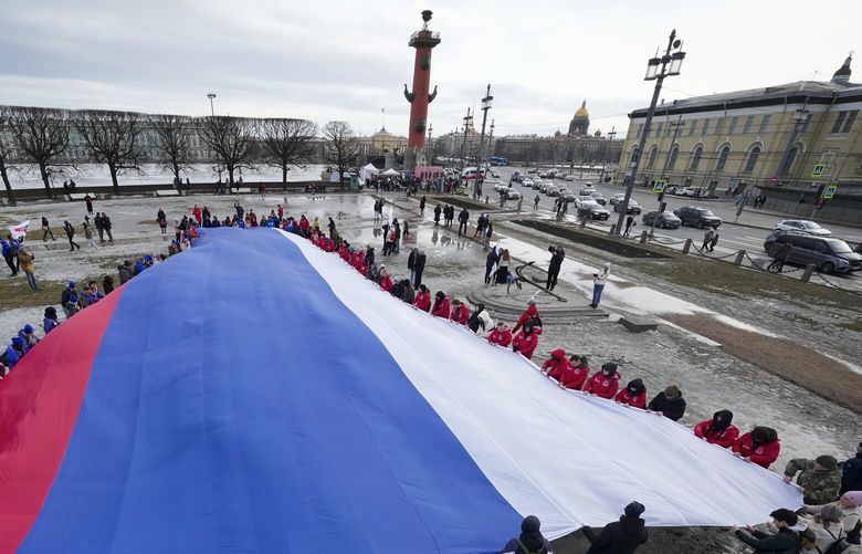 Young people unfurl a giant Russian flag during an action to mark the ninth anniversary of the Crimea annexation from Ukraine in St. Petersburg, Russia, Saturday, March 18, 2023. (AP Photo/Dmitri Lovetsky) XDL103 XDL103