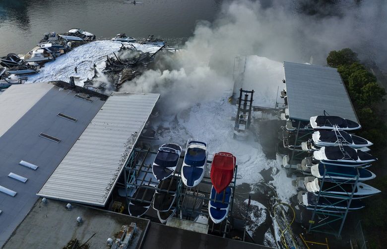 Smoke rises as fire fighters extinguish a blaze at a boat dry-storage facility, seen from the air in the Northlake area, during Wednesday morning  rush-hour, March 22, 2023, in Seattle. At left is the University Bridge.