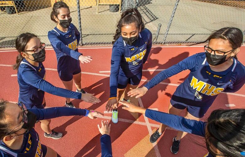 MONTEBELLO, CA – MARCH 11, 2021: Members of the Montebello High School girls cross country team are careful not to touch hands while wearing masks as they huddle up before a home meet against Bell Gardens High School. Montebello Unified starting to bring students back for athletic events. (Mel Melcon / Los Angeles Times) 75237991P