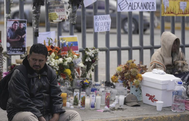A Venezuelan migrant sits on the sidewalk where an altar was created with candles and photos outside the Mexican immigration detention center that was the site of a deadly fire, as migrants wake up after spending the night on the sidewalk in Ciudad Juarez, Mexico, Thursday, March 30, 2023. (AP Photo/Fernando Llano) XLM103 XLM103