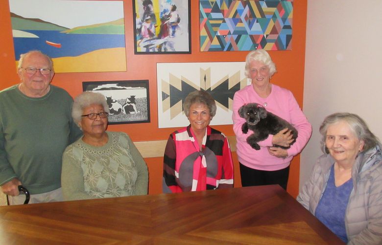 Participants in the programs at the Senior Center of West Seattle pose near a wall of art.