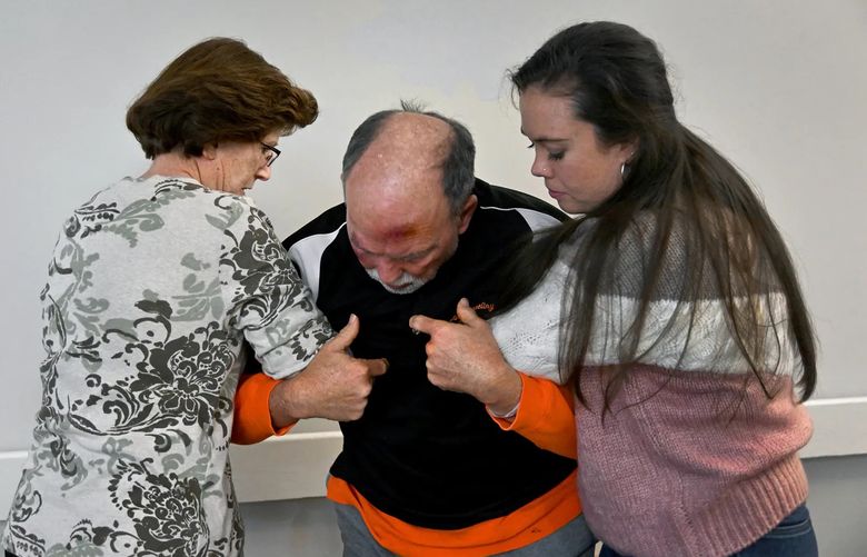 Beth Roper, left, helps her husband, Doug Roper, get comfortable on a bench with the assistance of their daughter, Kathyrn Roper, at a locked memory care facility in Poquoson, Va., where Doug Roper lives. He has Alzheimer’s disease, and his care costs nearly $6,000 a month. (Washington Post photo by Michael S. Williamson)