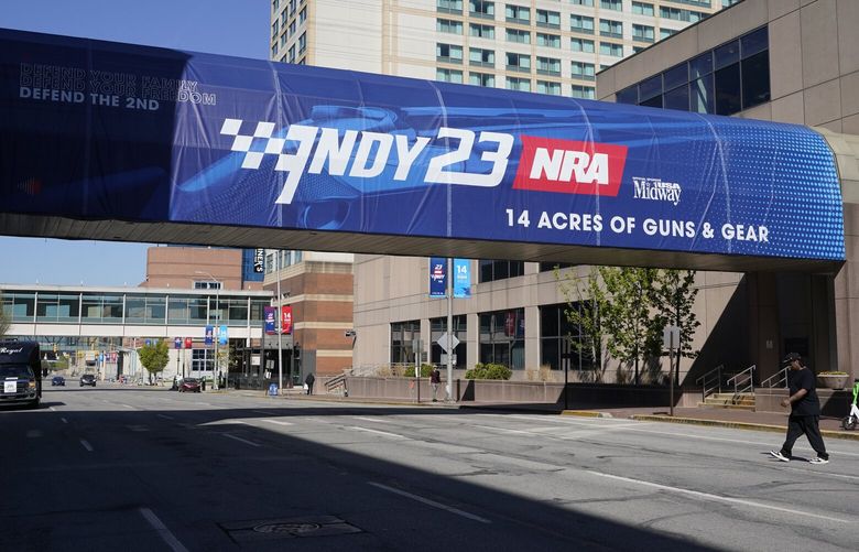 A pedestrian walks under a sign advertising the NRA Convention, Thursday, April 13, 2023, in Indianapolis. The convention starts Friday, April 14 and end on Sunday, April 16. (AP Photo/Darron Cummings) INDC101 INDC101