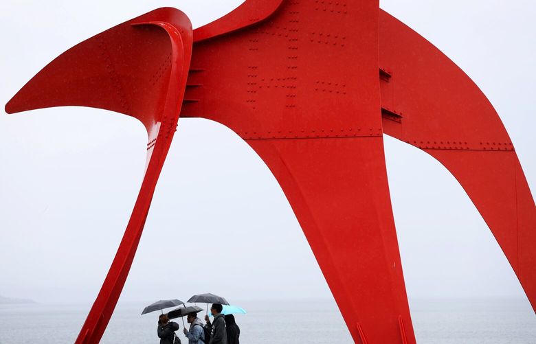 The drizzle is out and so are the umbrellas as Alexander Calder’s 1971 work “The Eagle” frames visitors looking out on Elliott Bay from the Seattle Art Museum’s Olympic Sculpture Park, Sunday, April, 9, 2023 in Seattle.