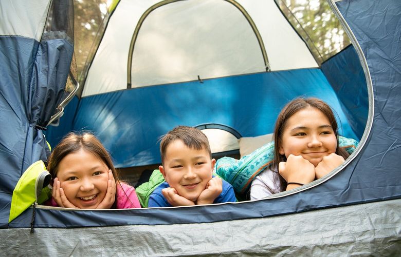 Three happy campers smile from their tent at a campsite in Deception Pass State Park. (Freya Fennwood / Washington State Parks)