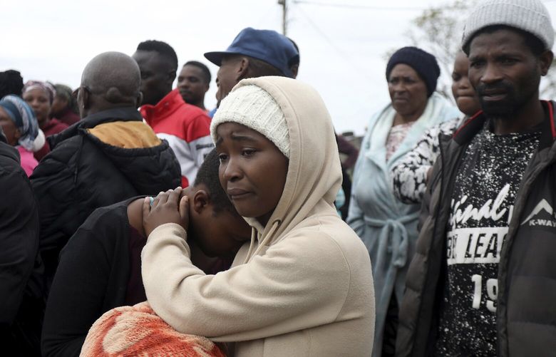 Neighbours comfort one another behind a police cordon where ten people from the same family were shot dead Friday, April 21, 2023. Police say 10 people were “ambushed” by unknown gunmen at a home in the city of Pietermaritzburg in the eastern KwaZulu-Natal province. (AP Photo) DUR102 DUR102