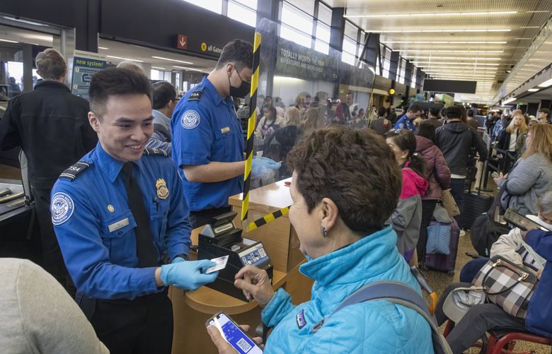 Aeron Vo, a first-line supervisor and lead TSA officer at Seattle-Tacoma International Airport, checks a passenger’s ID at a security checkpoint. (Ellen M. Banner / The Seattle Times)