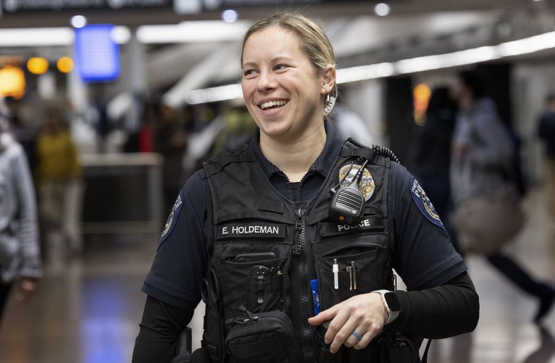 Emily Holdeman, a Port of Seattle police officer, watches as passengers pass by in the baggage claim area. She often answers questions and helps people as they pass through the airport. (Ellen M. Banner / The Seattle Times)