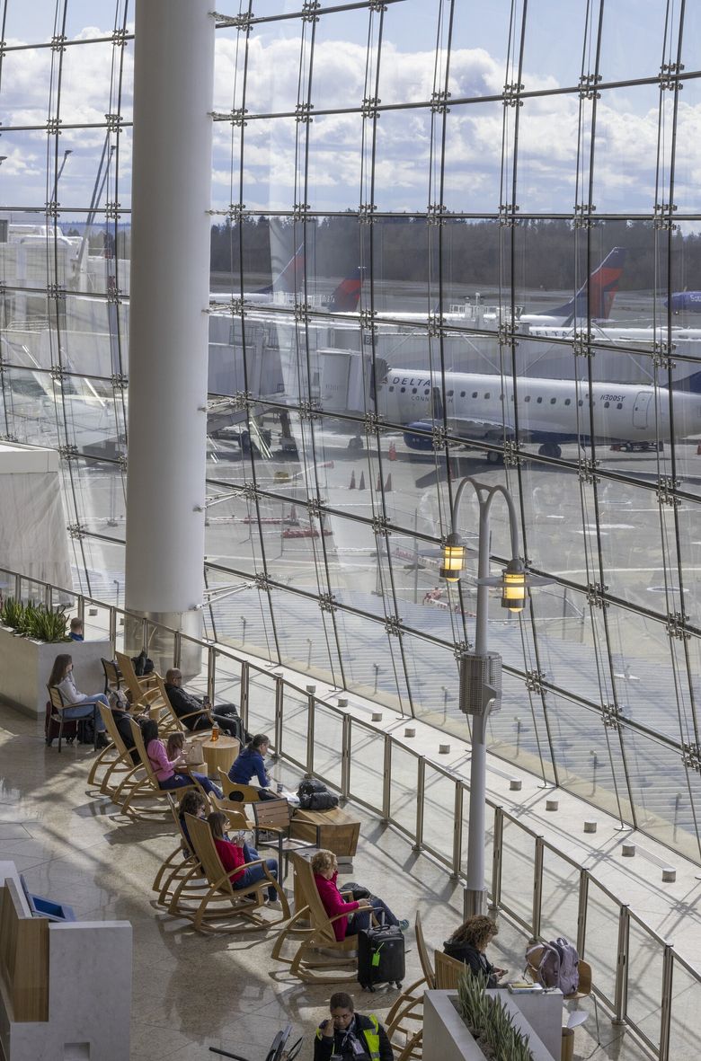 Travelers sit in rocking chairs as they watch planes on the tarmac and in the air at Seattle-Tacoma International Airport. (Ellen M. Banner / The Seattle Times)