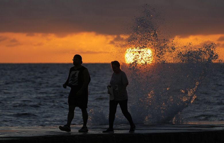 FILE – The sun rises above the Atlantic Ocean as waves crash near beach goers walking along a jetty, Dec. 7, 2022, in Bal Harbour, Fla. The world’s oceans have suddenly spiked much hotter and well above record levels, with scientists trying to figure out what it means and whether it forecasts a surge in atmospheric warming. (AP Photo/Wilfredo Lee, File) CLI701 CLI701