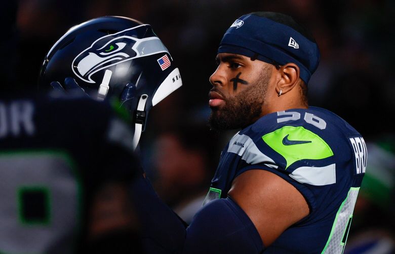 Seattle Seahawks linebacker Jordyn Brooks puts his helmet back on while standing in a patch of sunlight after the playing of the national anthem before the start of a game against the New York Jets.